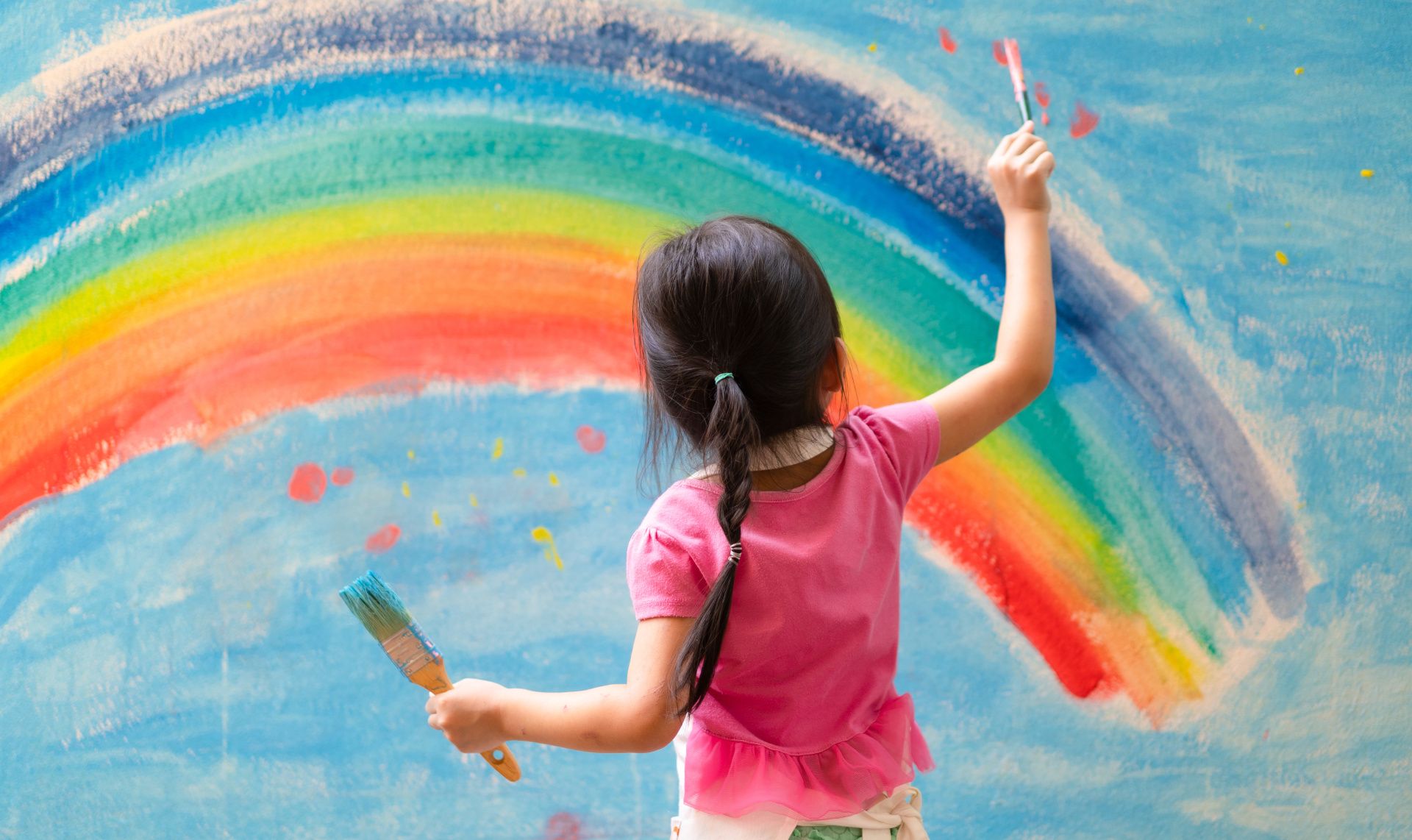 young girl painting rainbow on wall