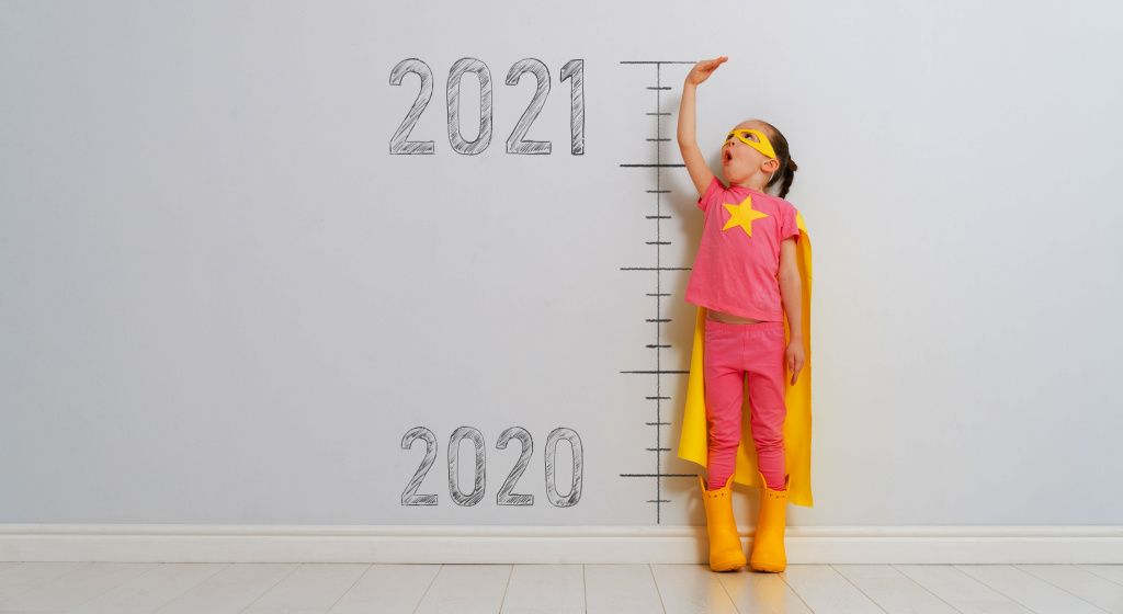 child in superhero costume standing tall by a growth chart