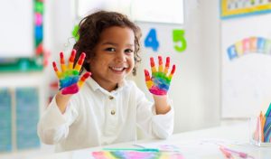 Nursery child showing hands covered in rainbow paint pattern
